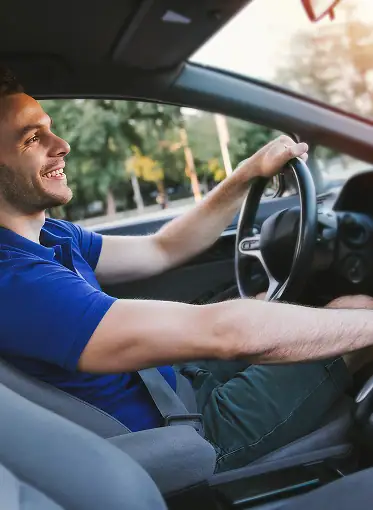Mann beim Autofahren während Fahrstunde, lachend und konzentriert.