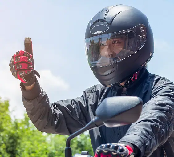 Fahrschüler auf Motorrad mit Schutzhelm, macht Handzeichen.